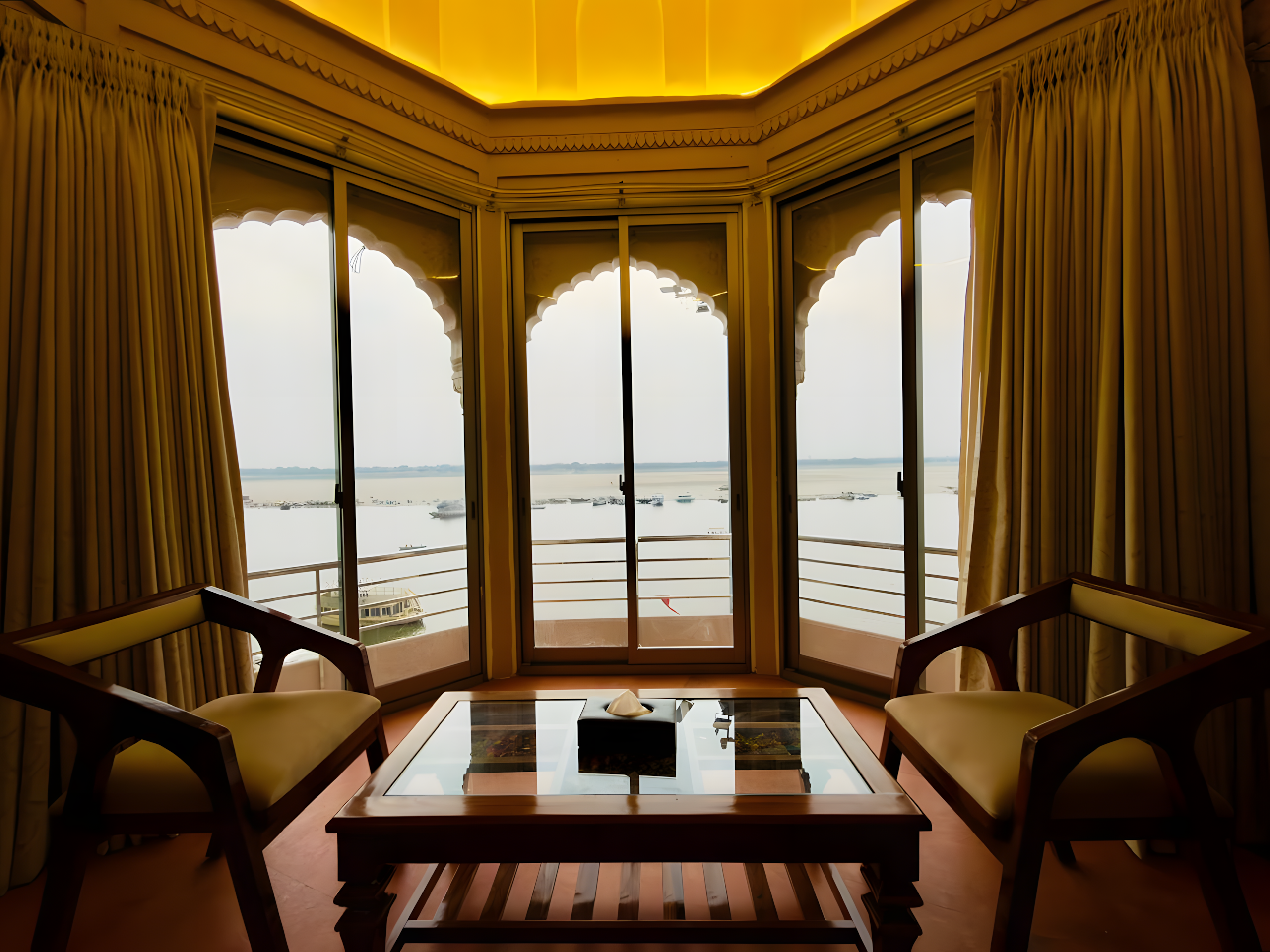 Kaashi Suite chhajja at Maharana Mahal boutique hotel Varanasi — golden octagonal bay window, Ganga river view with boats, carved Mughal arch frame — heritage palace hotel Banaras India