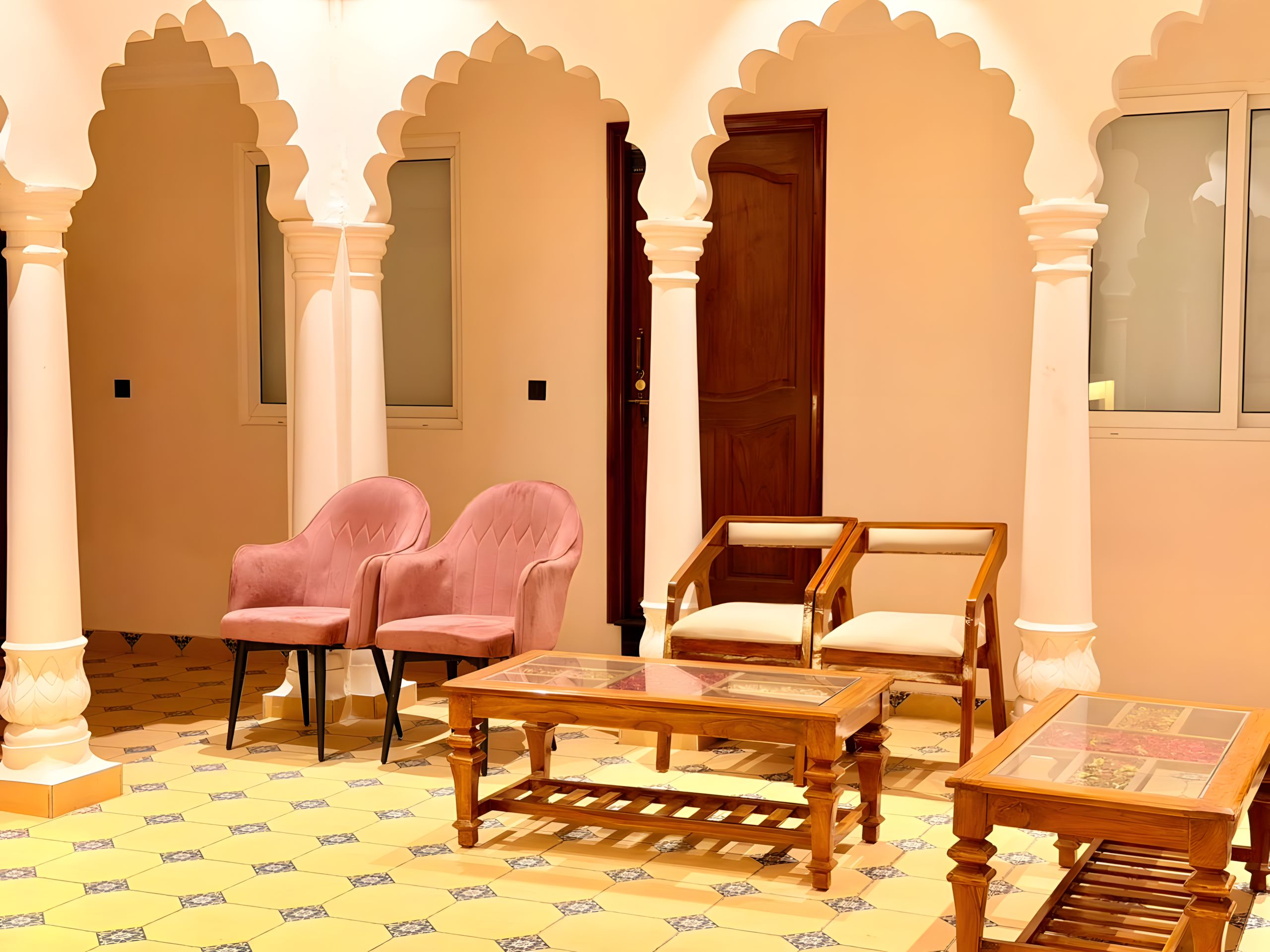 Palace corridor seating at Maharana Mahal heritage hotel Varanasi — pink velvet chairs, teak tables, carved white Mughal arches, Rajasthani mosaic tile floor — 17th-century Rajput palace hotel on the Ganges