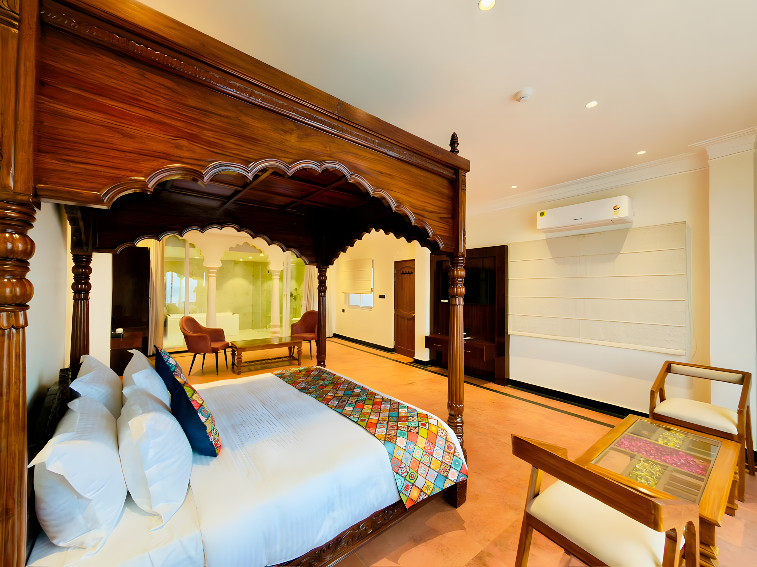 Ganga Darshan Suite at Maharana Mahal Varanasi — carved four-poster bed with Mughal arch canopy, Banarasi patchwork bedding, open arch view into tree-feature luxury bathroom — heritage palace hotel India