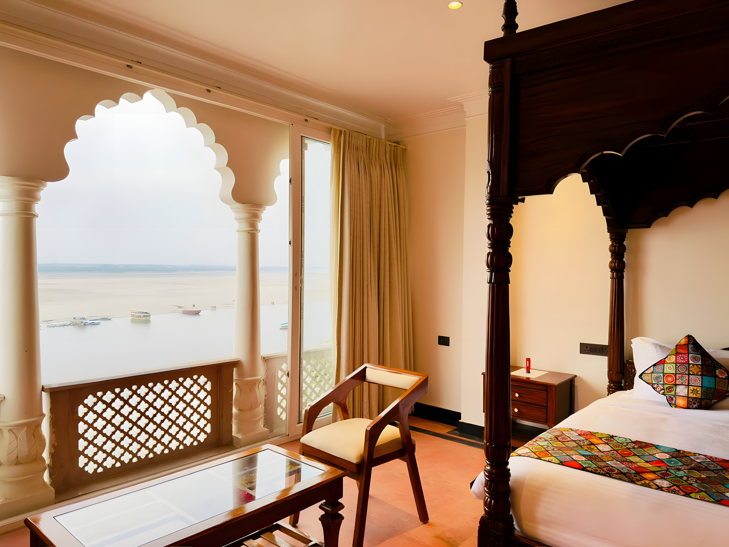 Kaashi Suite with Ganga view at Maharana Mahal Varanasi — four-poster heritage bed, open Mughal colonnade balcony with bench seating, sacred Ganges river in daylight — spiritual luxury hotel India