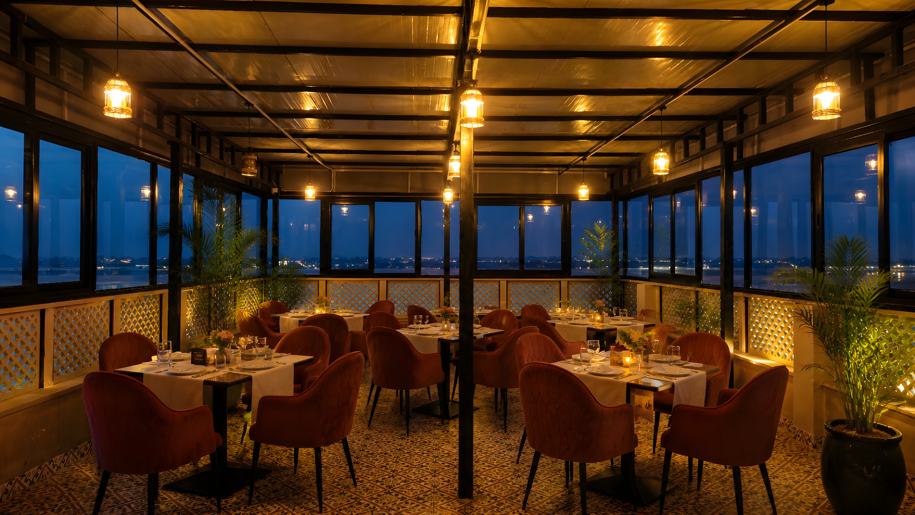 Kinara restaurant at Maharana Mahal luxury hotel Varanasi — elegant dining room with velvet chairs, candlelit tables, pendant lights and panoramic Ganga river view at night — best rooftop restaurant Varanasi