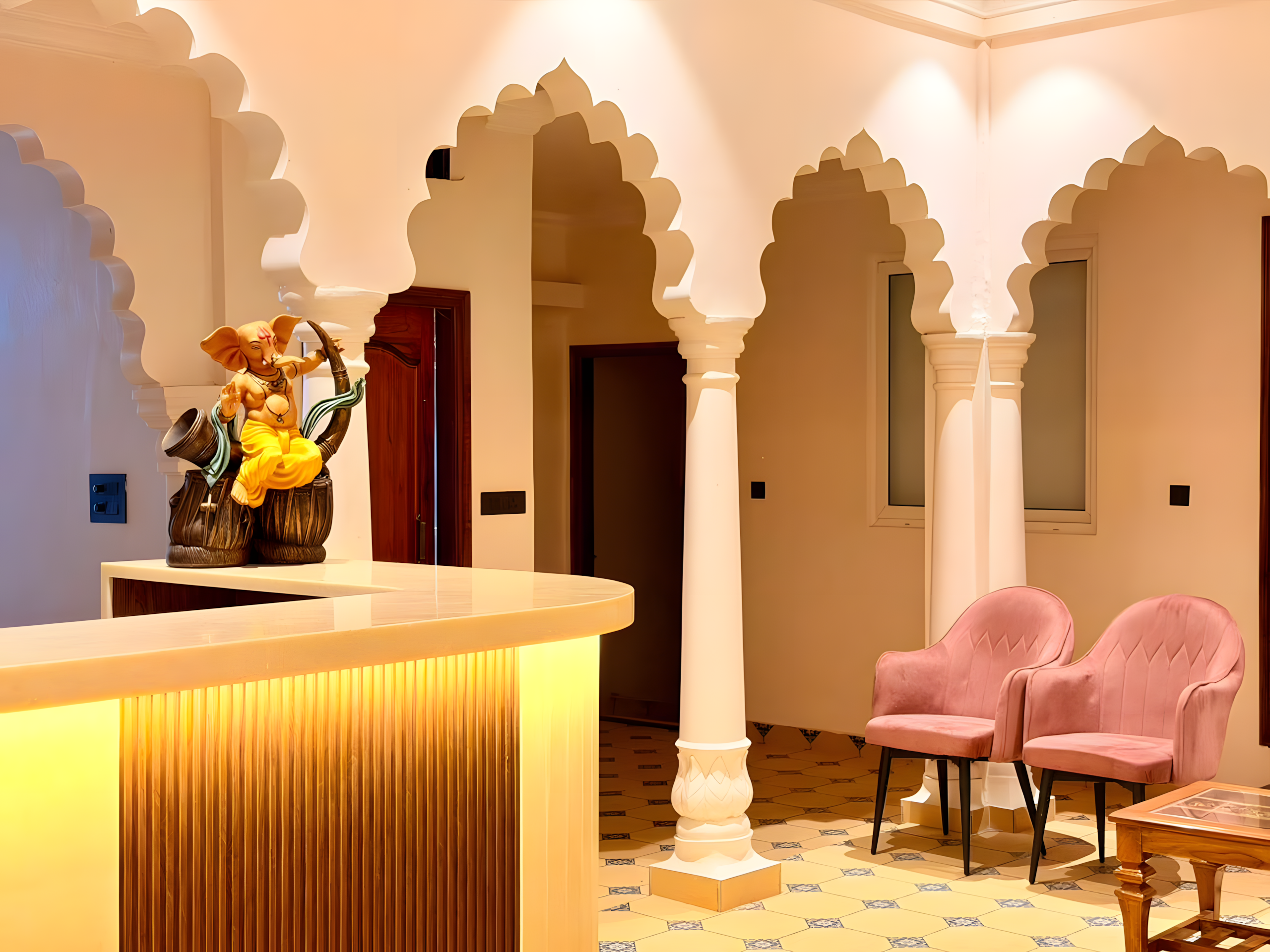 Hotel reception at Maharana Mahal heritage hotel Varanasi — Ganesha idol on illuminated front desk, pink velvet chairs, carved white Mughal arches, Rajasthani mosaic tile floor — spiritual boutique palace hotel Rana Mahal Ghat
