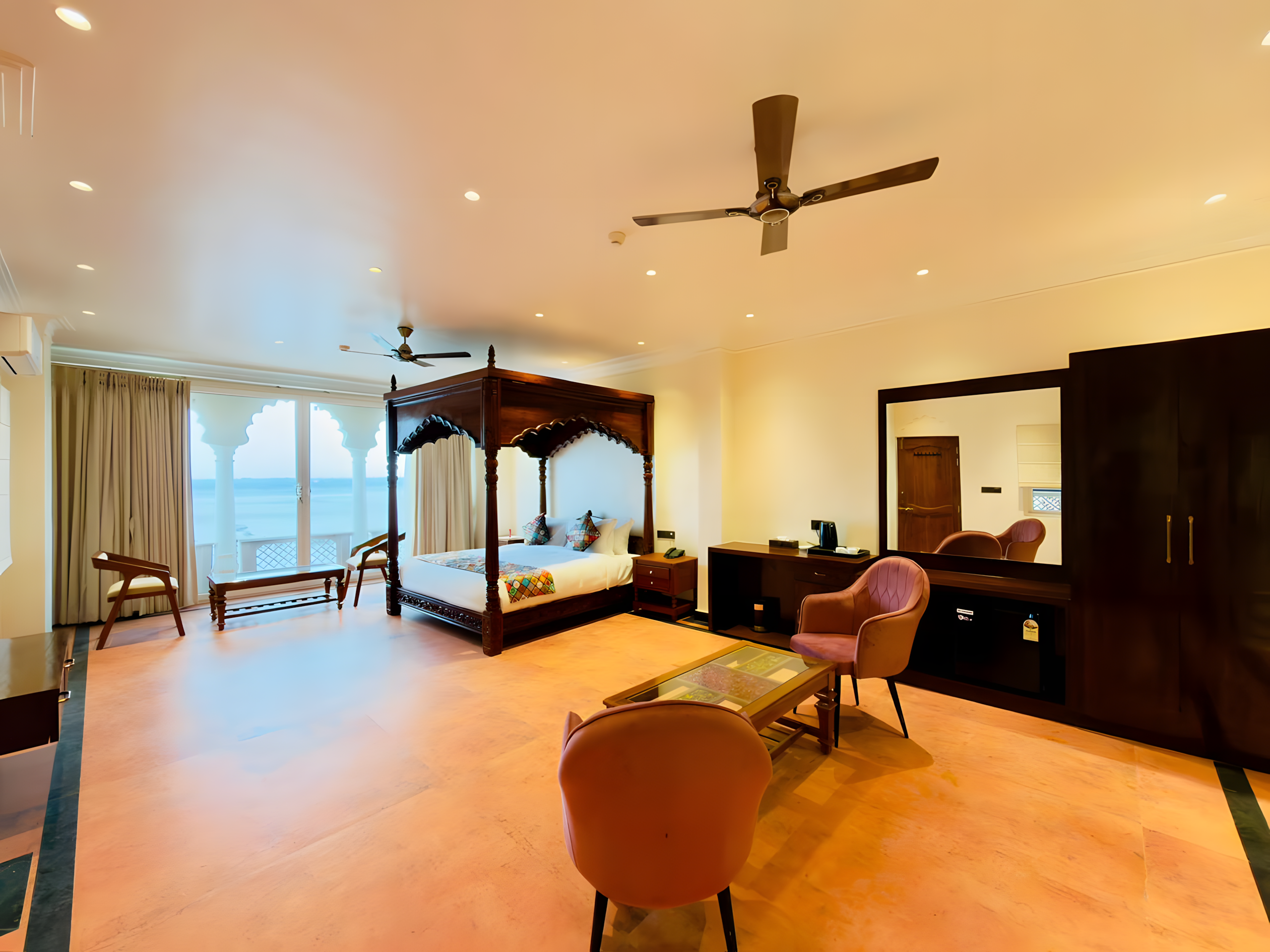 Ganga Darshan Suite at Maharana Mahal luxury hotel Varanasi — spacious room with carved four-poster teak bed, pink velvet chairs, and private chhajja balcony with direct Ganga river view