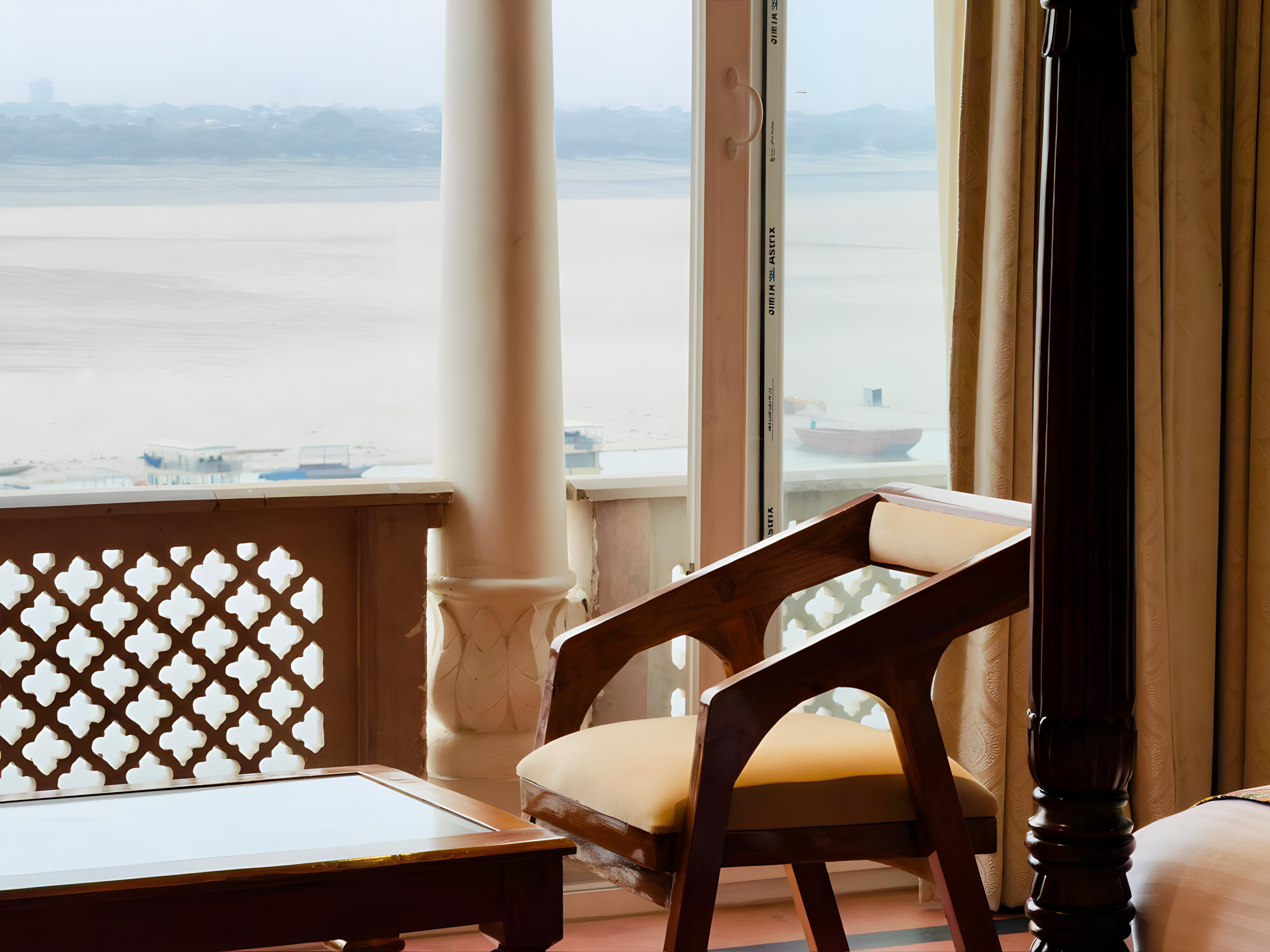 Ganga river view through carved Rajput jali screen and Mughal arch at Maharana Mahal Varanasi — four-poster bed post, boats on the Ganges visible below — luxury heritage hotel with Ganga view India